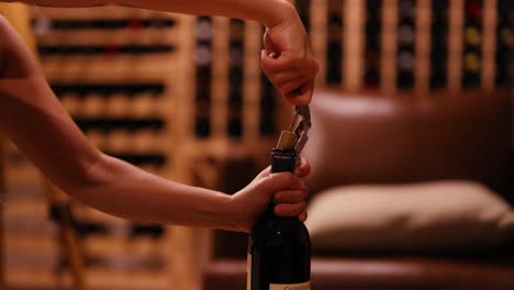 hands using a corkscrew to open a wine bottle in a warmly lit cellar with wooden shelves