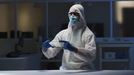 caucasian male medical worker wearing protective clothing and gloves using handheld interface in lab