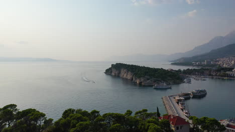 Makarska-city-port-at-sunset,-boat-and-jetski-arriving-at-harbour,-aerial-reveal