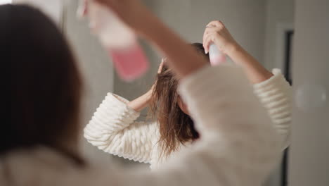 잘 관리 된 여성은 밝은 화장실에서 머리카락에 스프레이를 뿌립니다. 젊은 여성은 머리카락 관리 치료를 스프레이 수분 혈청을 느린 동작으로합니다.
