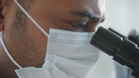 man in protective mask looking through microscope