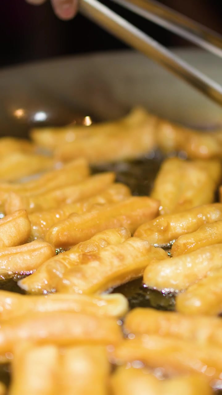 Primo piano di impasto patongko dorato che frigge in olio bollente, con pinze metalliche che girano i pezzi