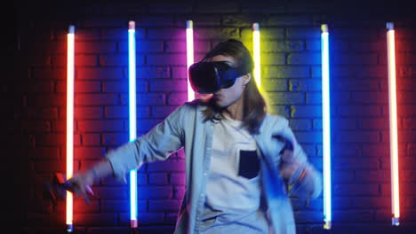 young man with long hair in vr glasses playing a game in a room with colorful neon lamps on the wall