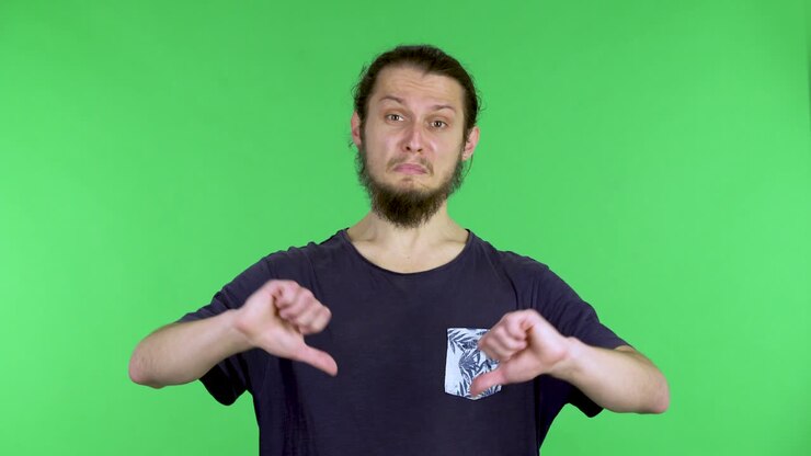Displeased young man, shows two thumbs down and shakes his head in disappointment. Refusal reaction, thumbs down, disgruntled guy. A man in the studio on a green screen. Close up