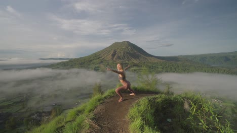 mujer en forma en pose de guerrero en el borde de la montaña con vistas al paisaje tropical, luz del sol de la mañana