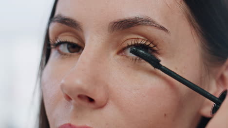 mujer de primer plano aplicando pestañas máscara maquillaje en el interior. pov rostro de mujer seria