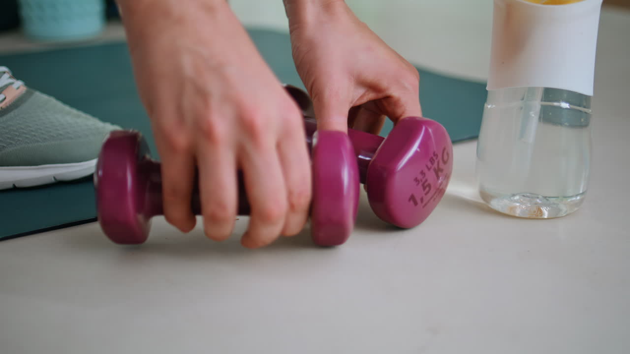 Sportswoman hands putting dumbbells on yoga mat near water bottle closeup