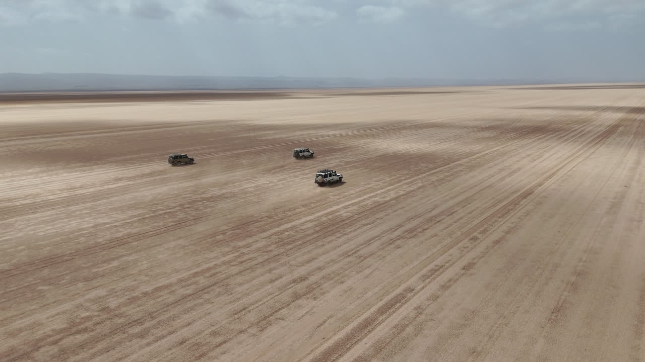 Riprese con drone di veicoli che attraversano un vasto paesaggio desertico con terreno accidentato e scie di polvere. Gibuti, Africa.