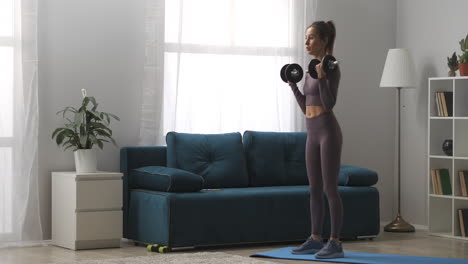 Entrenamiento-Diario-En-Casa-Joven-Atlética-Está-Entrenando-Con-Pesas-En-La-Sala-De-Estar-Durante-El-Día-Retrato-Completo-De-Una-Deportista-En-Un-Interior-Moderno-Estilo-De-Vida-Saludable