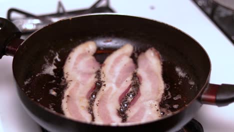 a time lapse or hyperlapse of preparing bacon in a hot frying pan