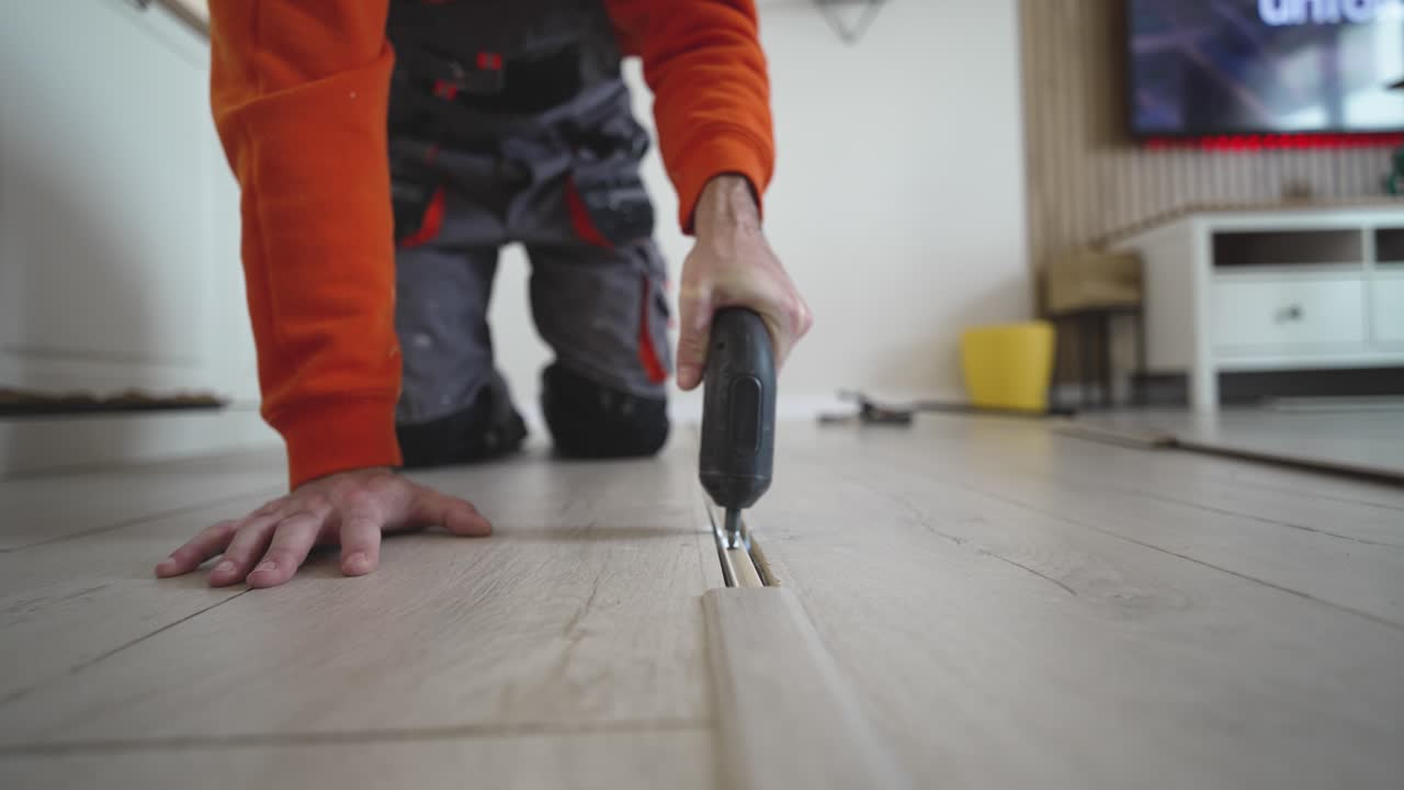 Focused man works on the floor using a screwdriver to secure a transition strip, capturing DIY flooring repair, home improvement, and interior maintenance