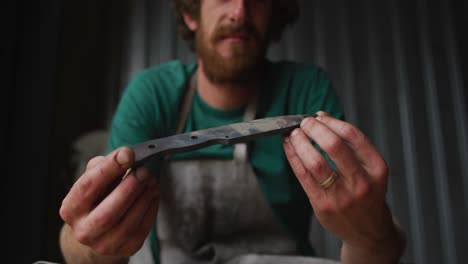 hombre caucásico herrero sosteniendo una herramienta de metal en el taller