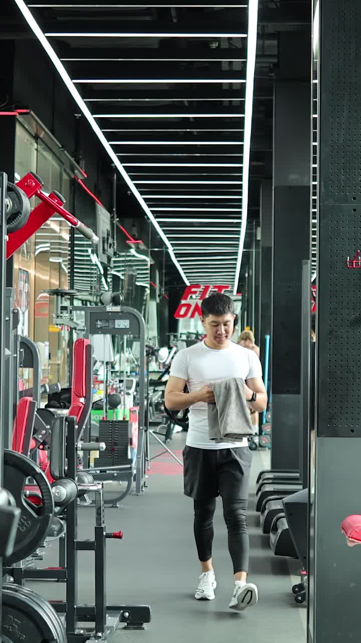Dua pria muda Asia berjalan melalui gym modern sambil membawa tas setelah berolahraga.