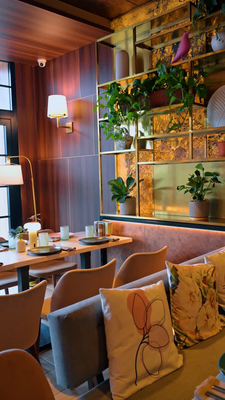 Interior de restaurante moderno com paredes de madeira e prateleiras decorativas. Vista de uma área de jantar com painéis de parede de madeira, prateleiras douradas com plantas e uma mesa posta com luminárias.