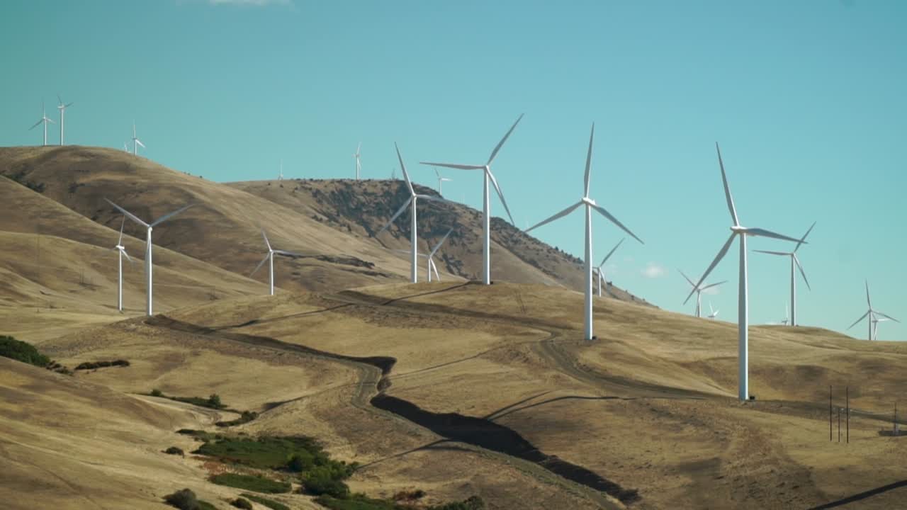 Windmills turn slowly on a golden brown hillside against an azure blue sky