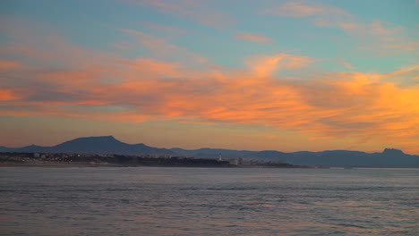 Cinematic-stunning-still-dramatic-bright-orange-clouds-sunset-dusk-lighthouse-Biarritz-Hossegor-France-beach-mountain-coastal-landscape-Biarritz-Basque-Country-city-lights-calm-water-bay