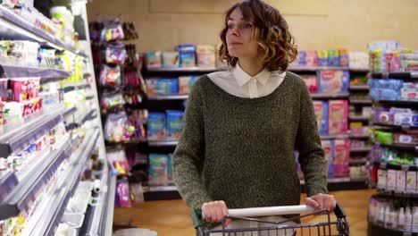 Food,-Health-Concept---Woman-in-a-supermarket-standing-in-front-of-the-freezer-shelves-and-choose-buying-a-bottle-of-yogurt