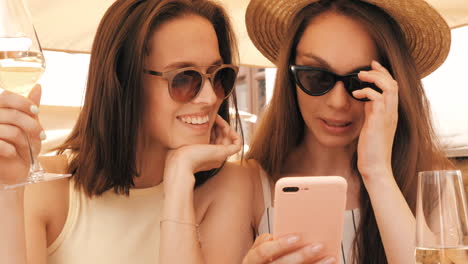 two women friends enjoying wine and looking at phone in a cafe