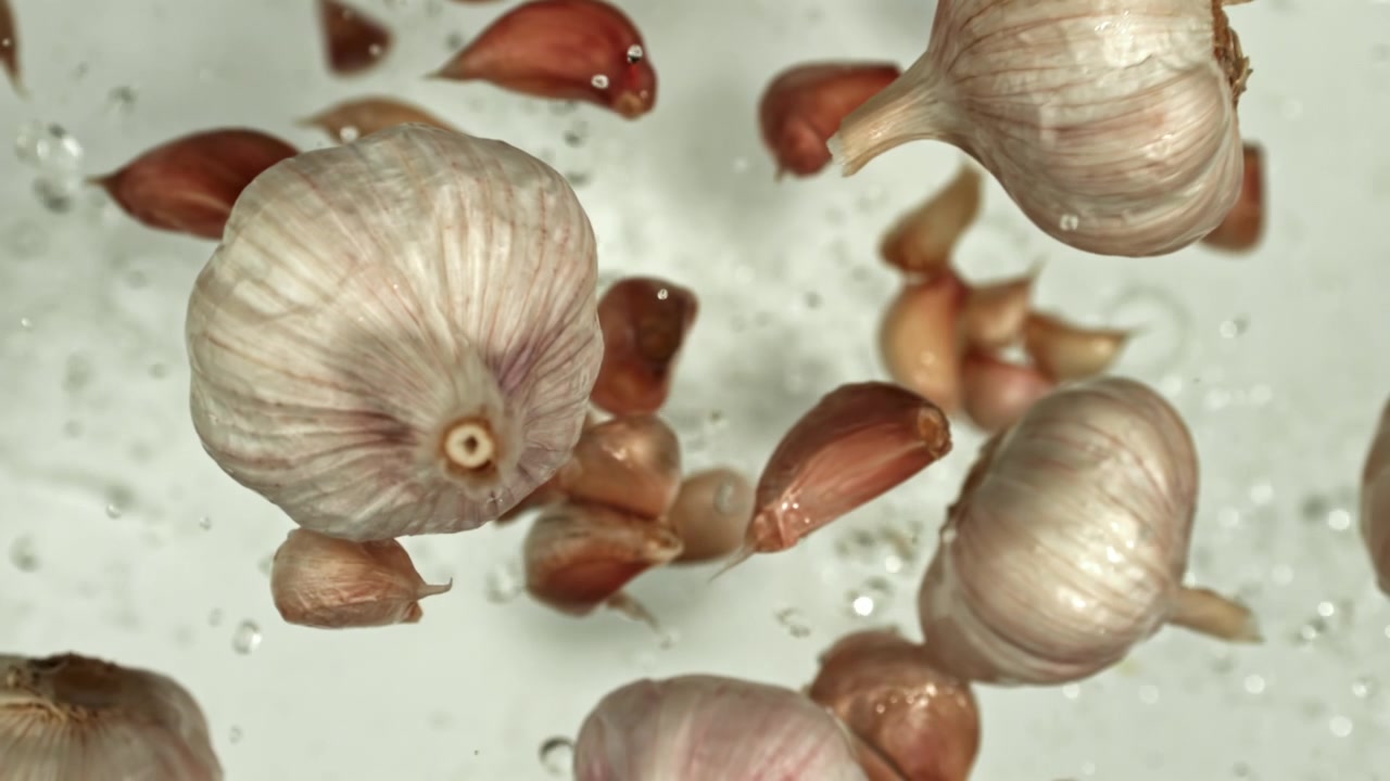 Bulbi e spicchi d'aglio che cadono al rallentatore con goccioline d'acqua