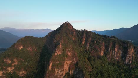 Drone-view-in-Guatemala-flying-in-front-of-a-green-mountain-face-shaped-surrounded-by-volcanos-at-sunrise-in-Atitlan