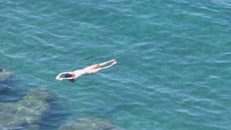 person swimming in the sea near rocks