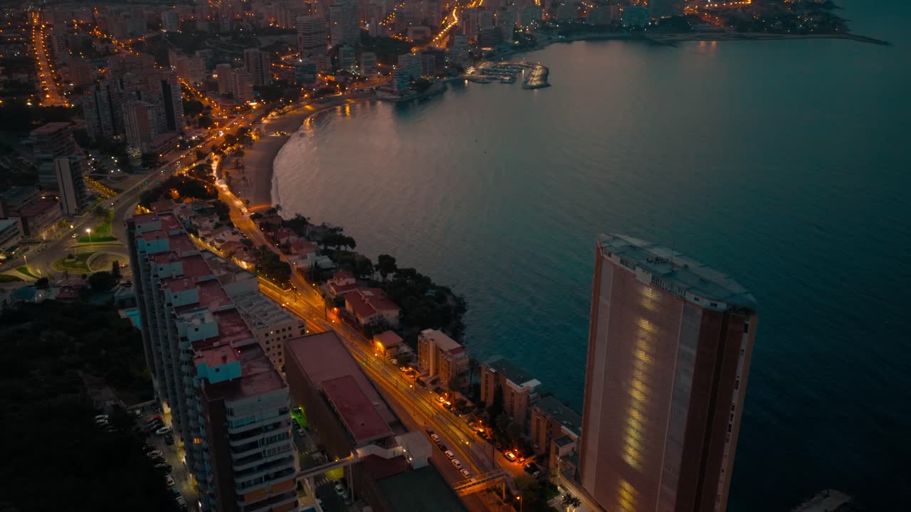 Città costiera spagnola ripresa di notte dall'alto con edifici, strade, auto, mare e una spiaggia.