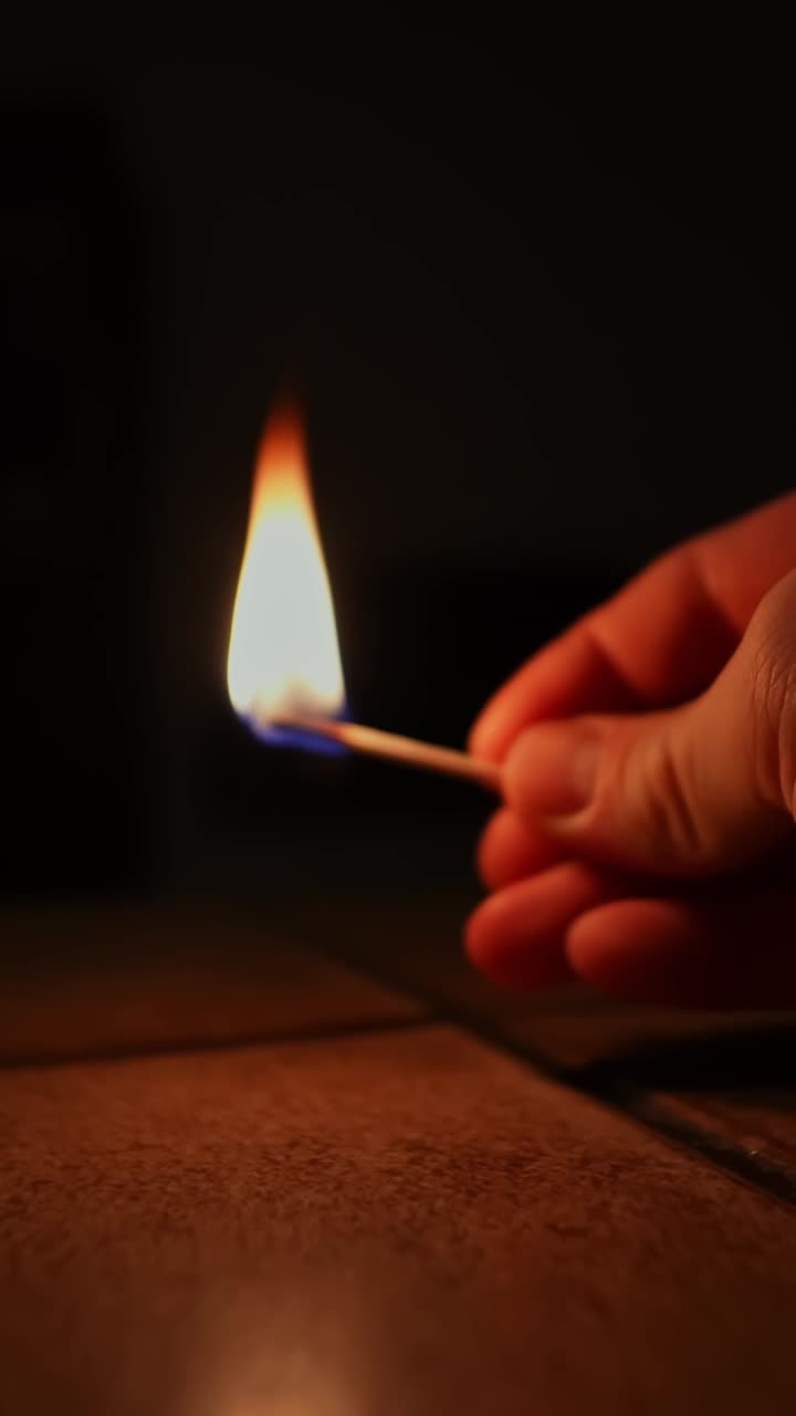 Una mano enciende una cerilla en una habitación oscura, creando un brillo cálido