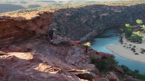 man hikes away, disappears around ochre cliff over gorge