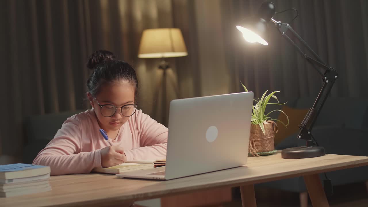 Teenage Girl With Laptop Doing Homework At Table In Evening