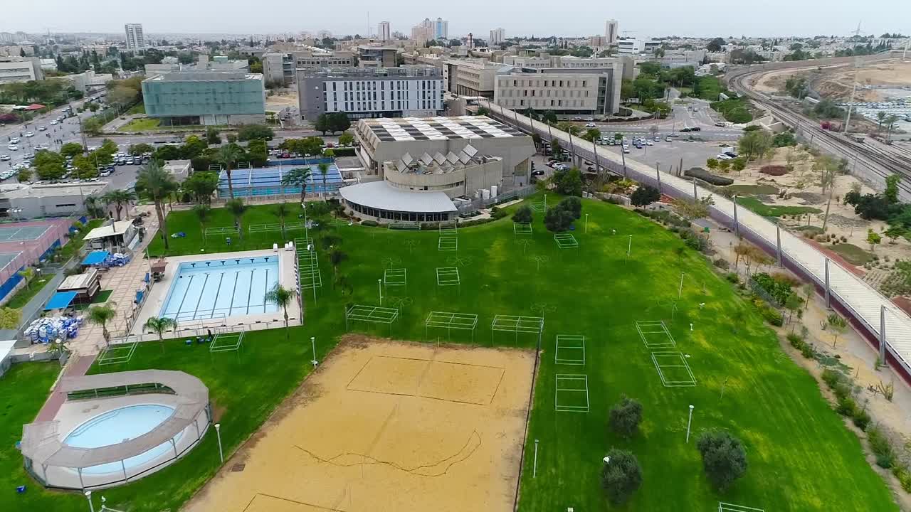 Take drone aerial over a pool area and sports spaces.