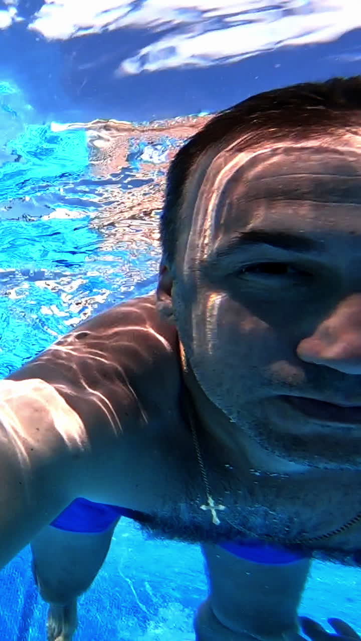 Healthy male is diving in blue water. A man swimming under the clear water with camera inside the pool. Underwater concept. Vertical video