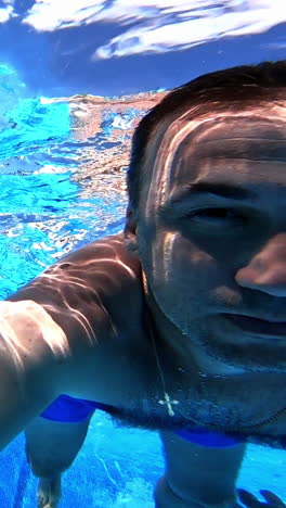 healthy male is diving in blue water. a man swimming under the clear water with camera inside the pool. underwater concept. vertical video
