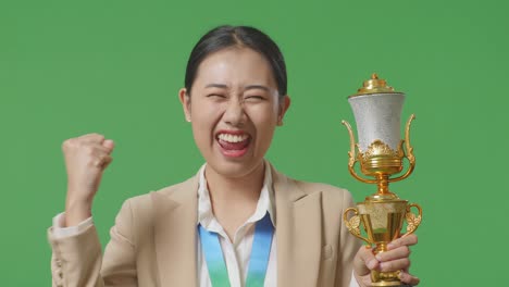 close up of asian business woman in a suit with a gold medal and trophy screaming goal celebrating winning as the first winner on green screen background in the studio