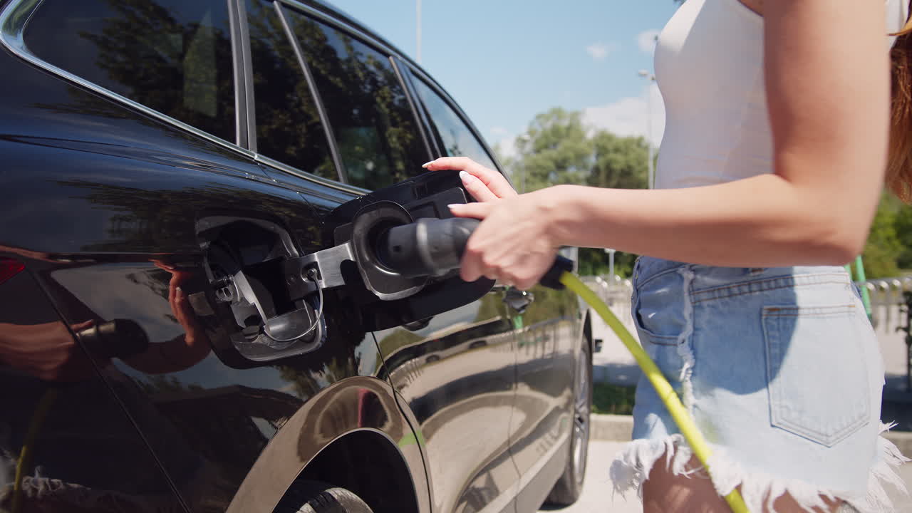 mujer cargando un coche ev en un estacionamiento de vehículos eléctricos, disparo de mano