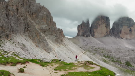drone circles person standing at edge looking out to tre cime di lavaredo mountain with distinct rugged spires in dolomites