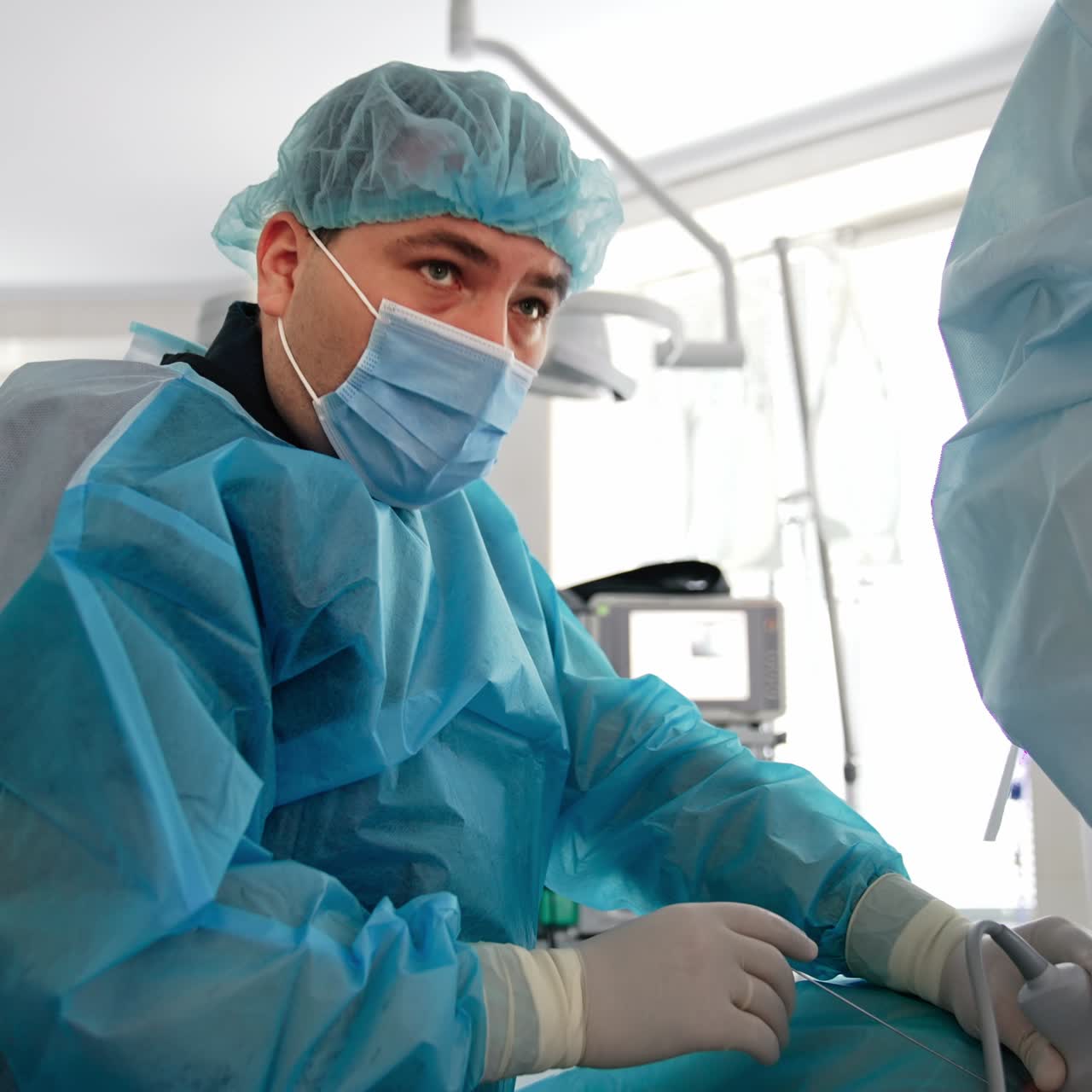 Surgeon holds an ultrasound device with one hand and inserts metal instrument with another. Doctor looks intently straight ahead on the screen