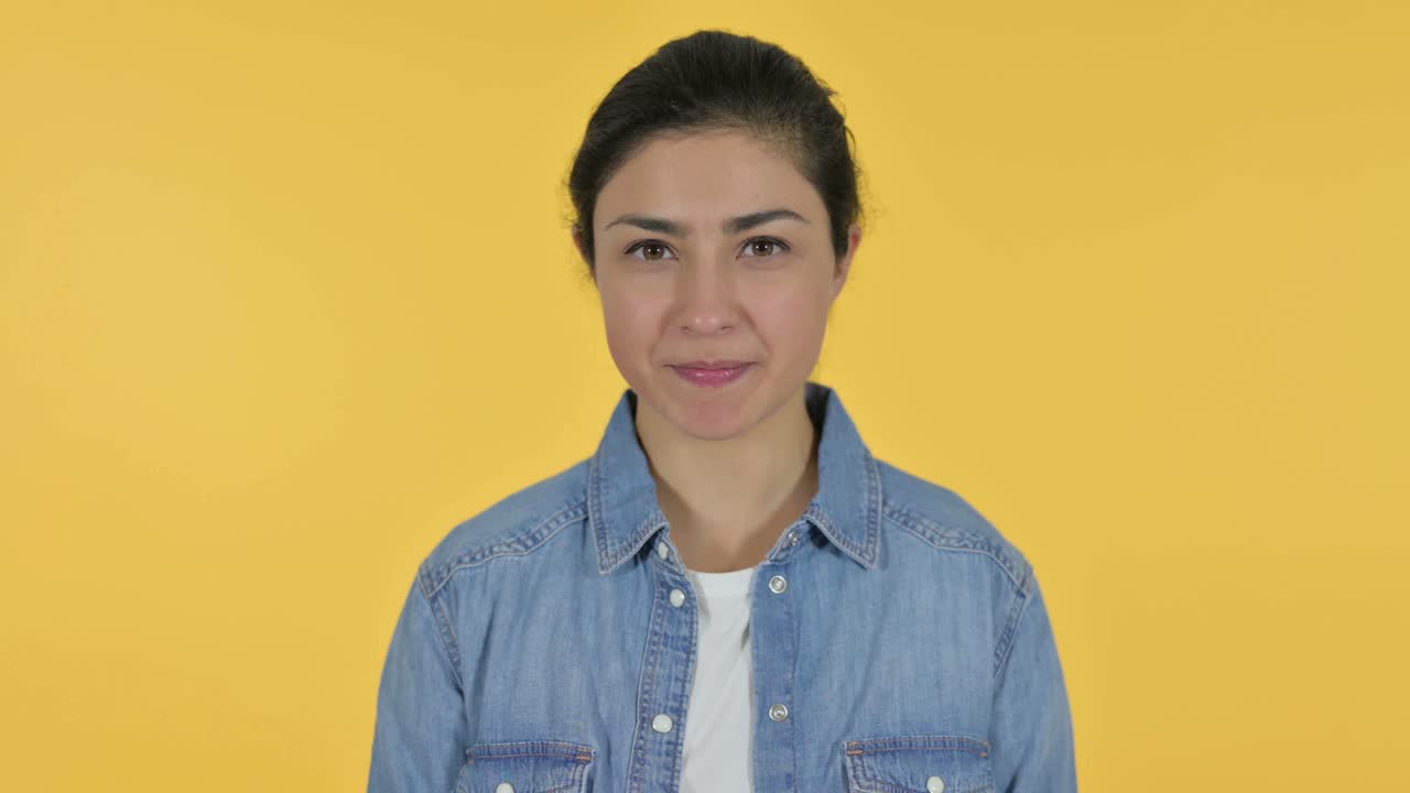 엄지손가락을 내려놓은 젊은 인도 여성, 노란색 배경