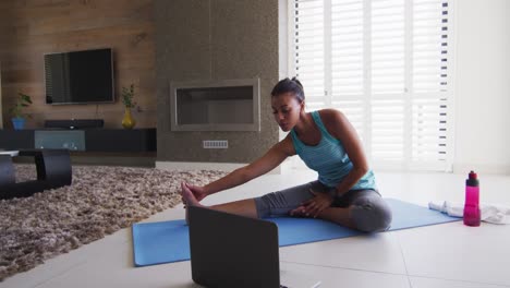 mixed race woman excercising on a mat with laptop