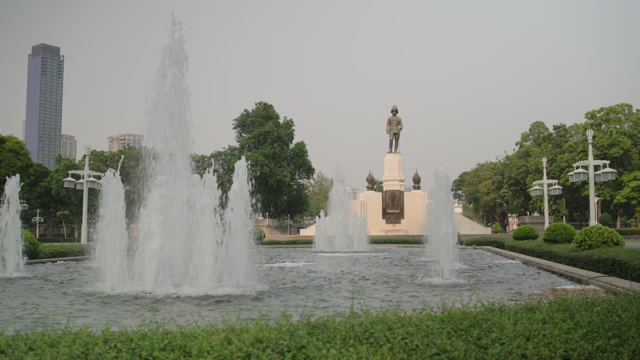 Fountain and statue in Bangkok park on a sunny day, serene cityscape view