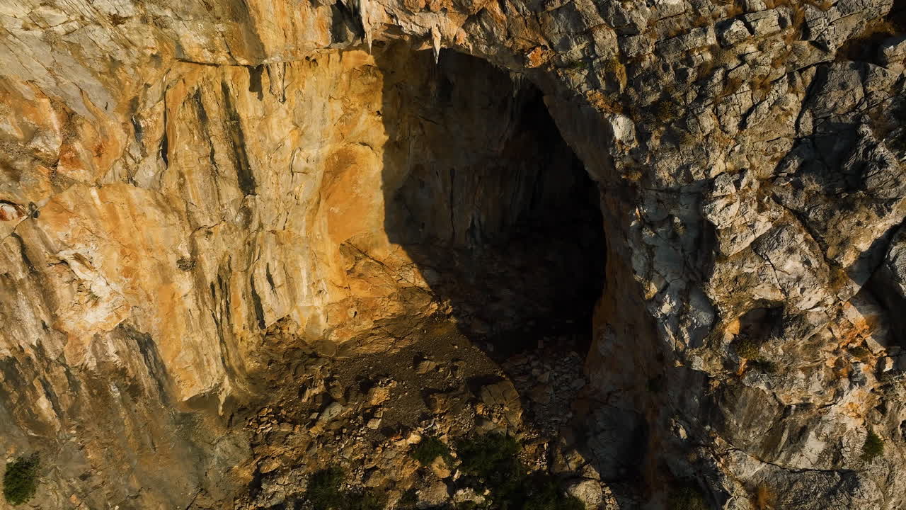 Drone rotating around a grotto carved in a mountain wall, golden hour in Greece