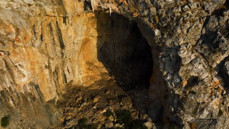 drone rotating around a grotto carved in a mountain wall, golden hour in greece