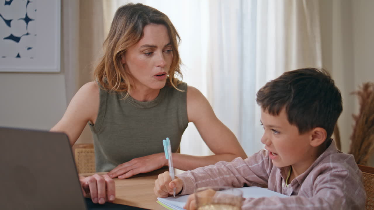 Closeup mom teaching son doing homework together in living room. Woman and child