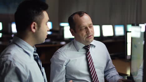 two men in shirts and ties discussing financial results in front of a computer screen