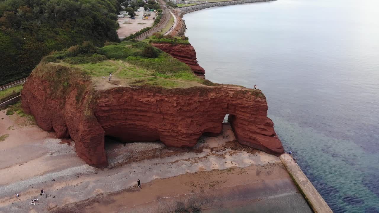Drone capture of Dawlish's iconic red sandstone cliffs surrounded by scenic ocean views. Push Forward, Tilt Down