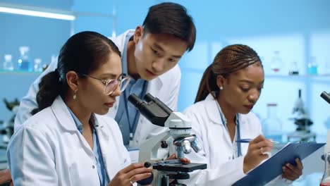 a diverse team of scientists, women and a man, in lab coats, work together using microscopes