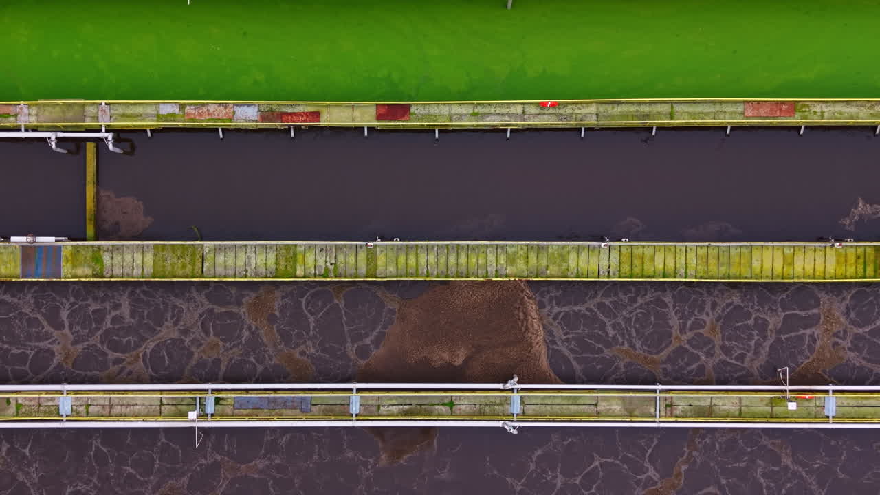 Water treatment facility shows different stages of water processing in large tanks with industrial structures in clear view during daylight hours