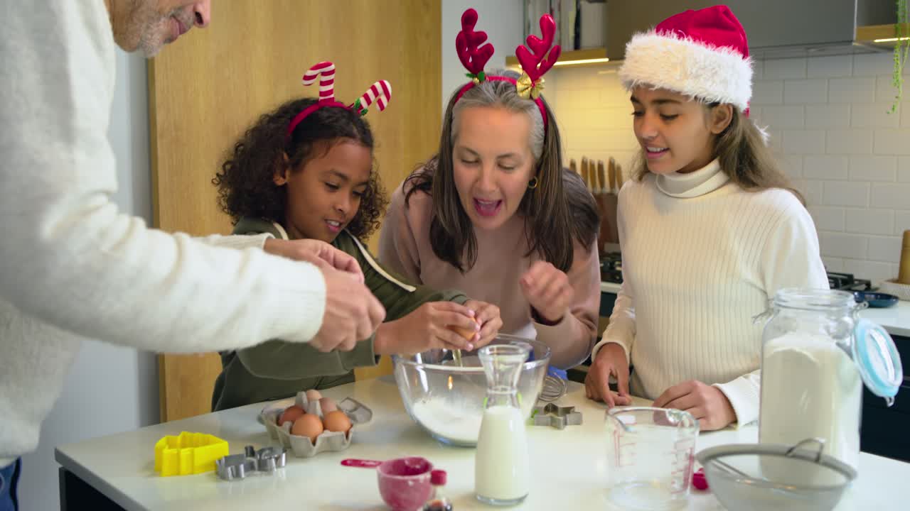 Diverse family gathering around holiday kitchen island sifting flour, cracking eggs in bowl