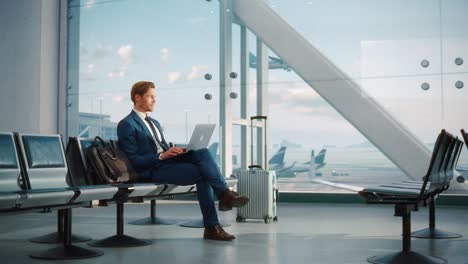 terminal de aeropuerto moderno: hombre de negocios guapo trabajando en una computadora portátil mientras espera su vuelo. hombre sentado en una sala de embarque de un gran centro de aerolíneas con aviones que salen y llegan