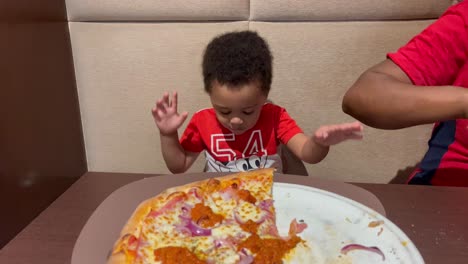 exotic and adorable two year old kid eating pizza for the first time inside a restaurant, seated next to mum, both of them wearing red shirts