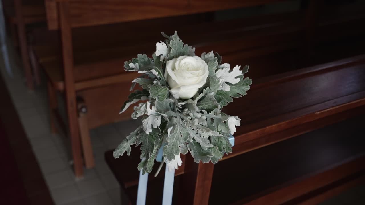 白いバラとシルバーリーフが、結婚式や洗礼式のために木製の教会のベンチを飾る。